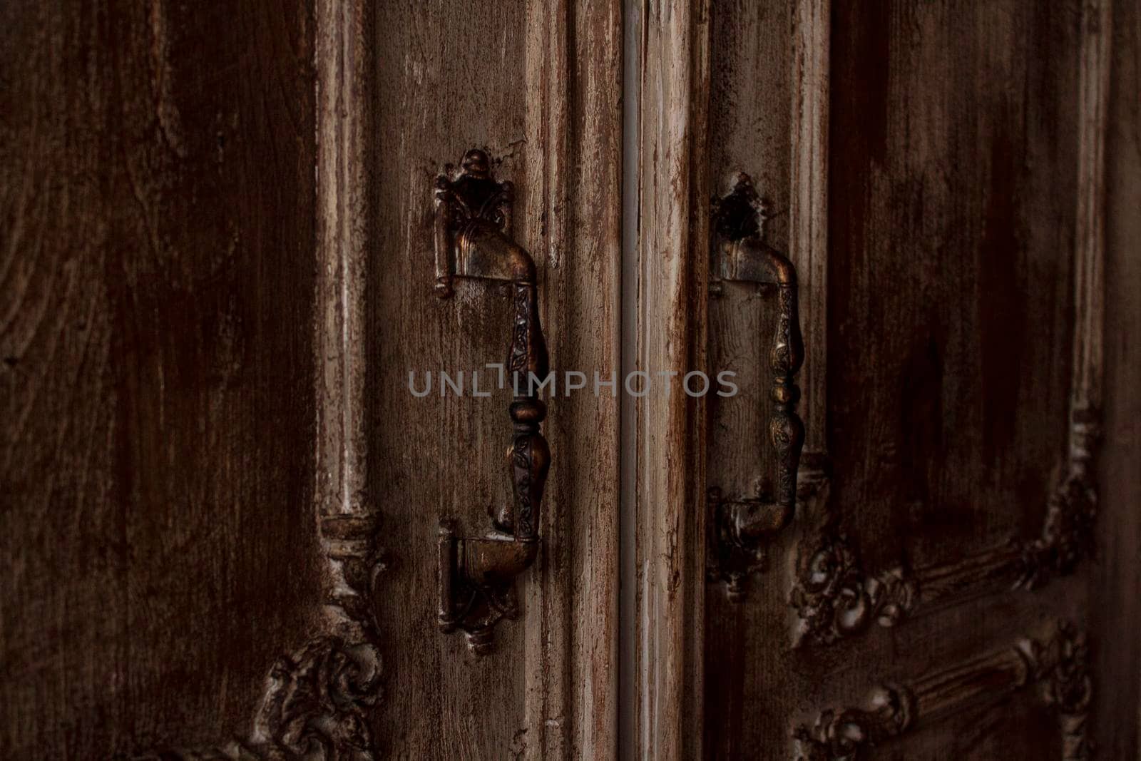 Door handles with an old double door. Entrance door with brass handle. Copper door handle in classic style on brown wood. Close-up of double antique doors by Hitachin