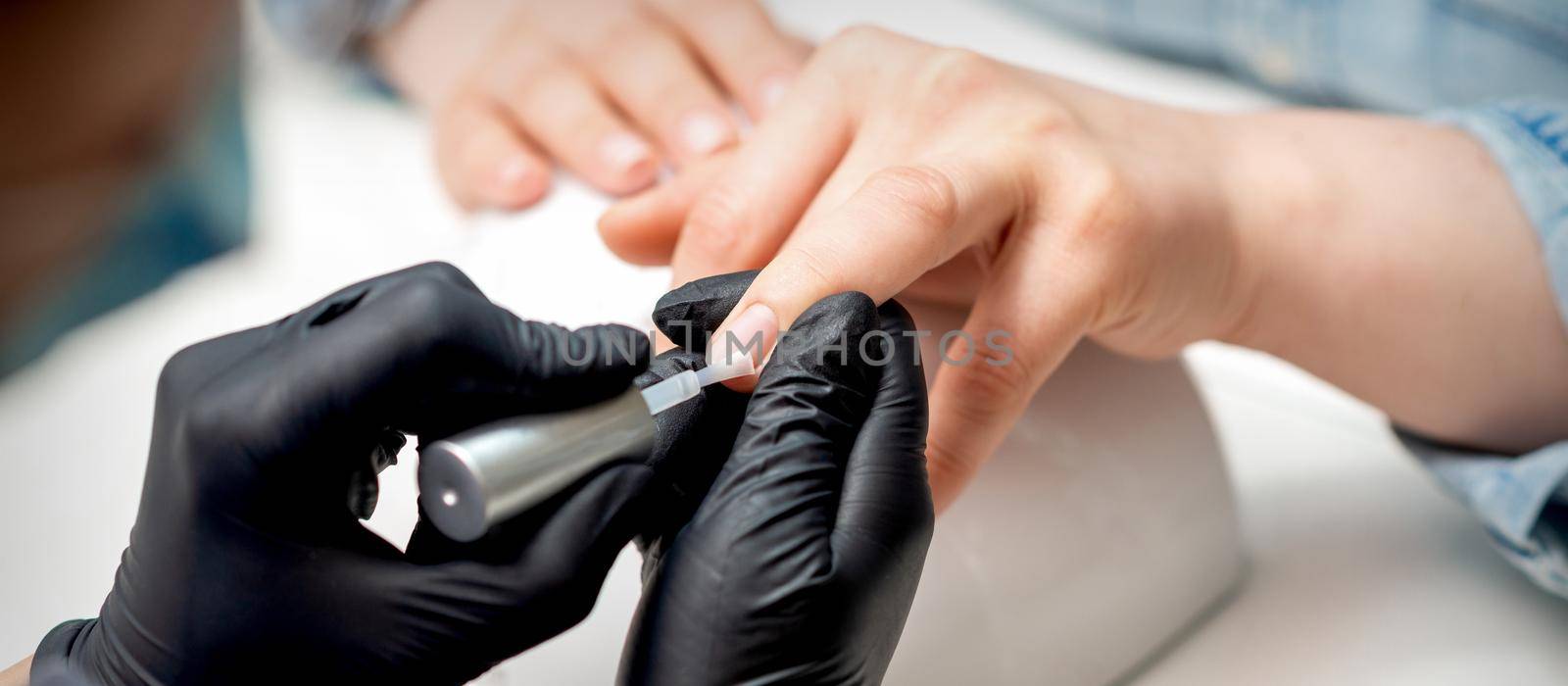 Manicure master is applying transparent varnish on female nails in nail salon