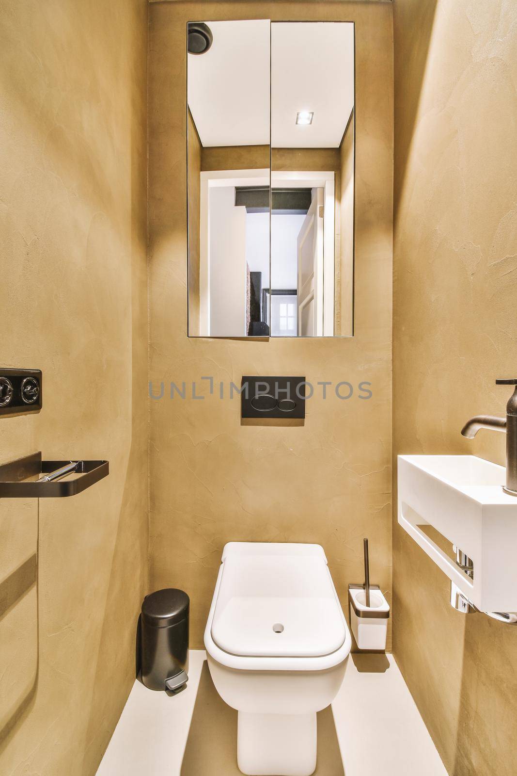 The interior of a modern toilet with beige walls, a small white sink and a cabinet with mirrored doors