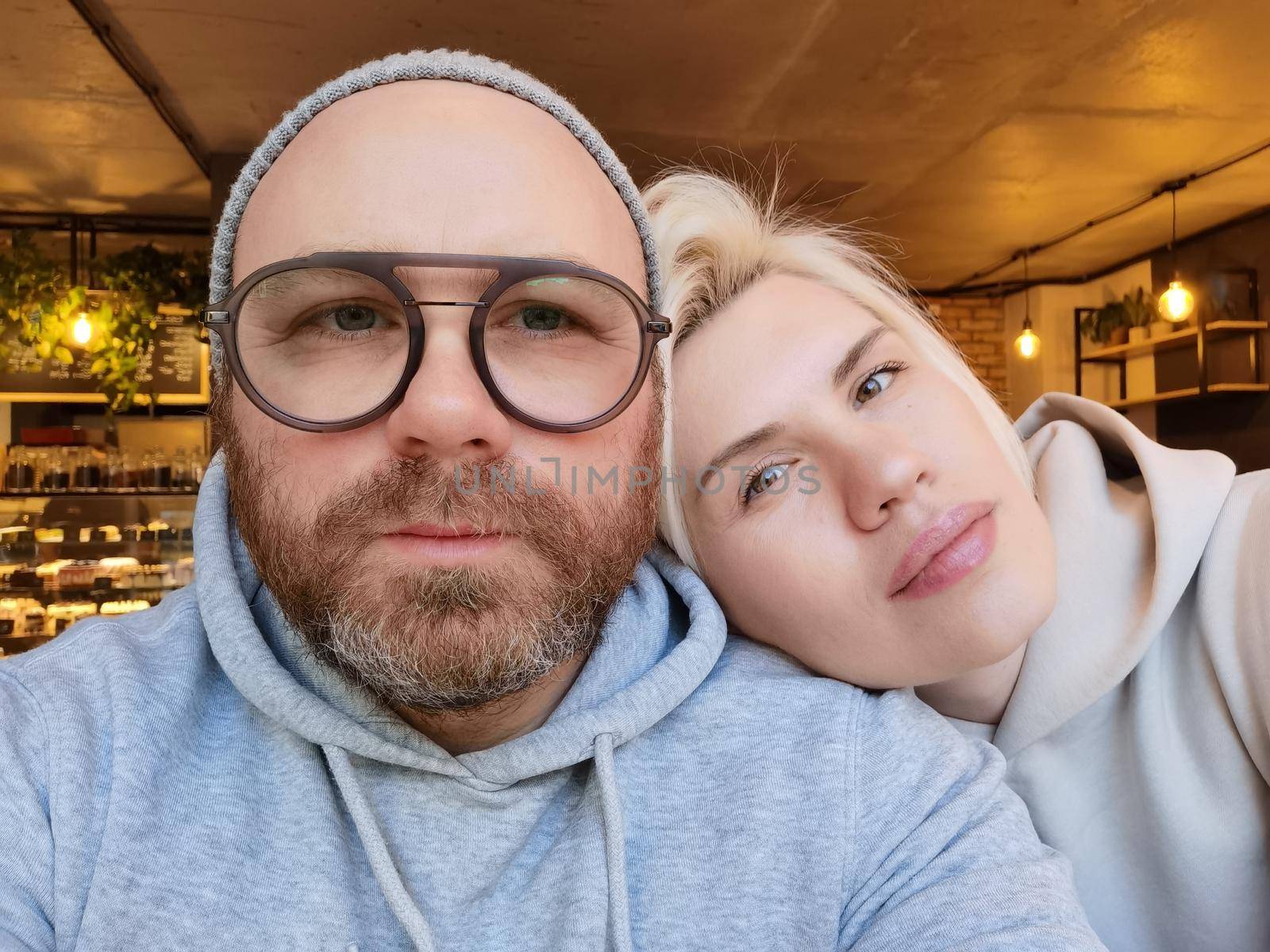 Romantic couple taking selfie in cafe. Young attractive man in eyeglasses with pretty blond woman. Restaurant or cafe
