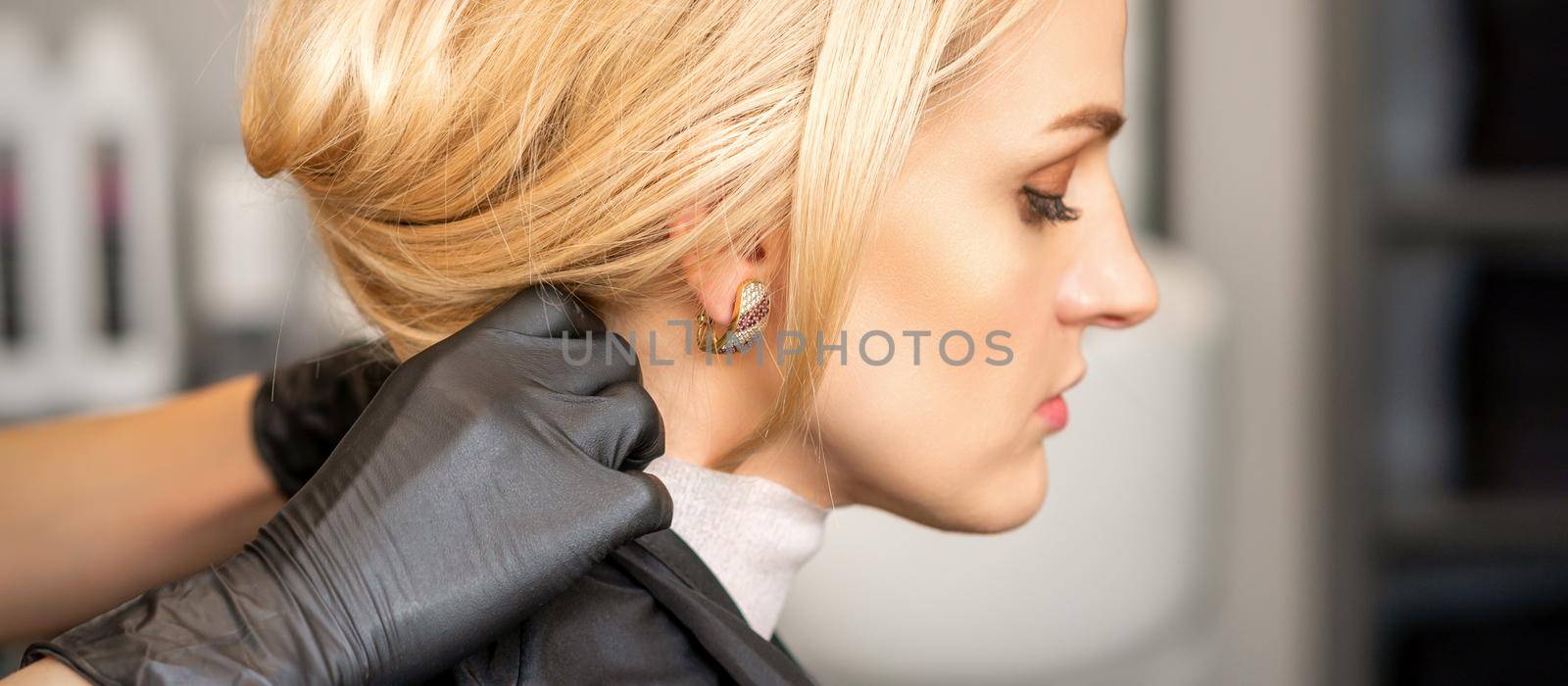 Hands of hairdresser making preparation before giving haircut to young blond woman at beauty salon