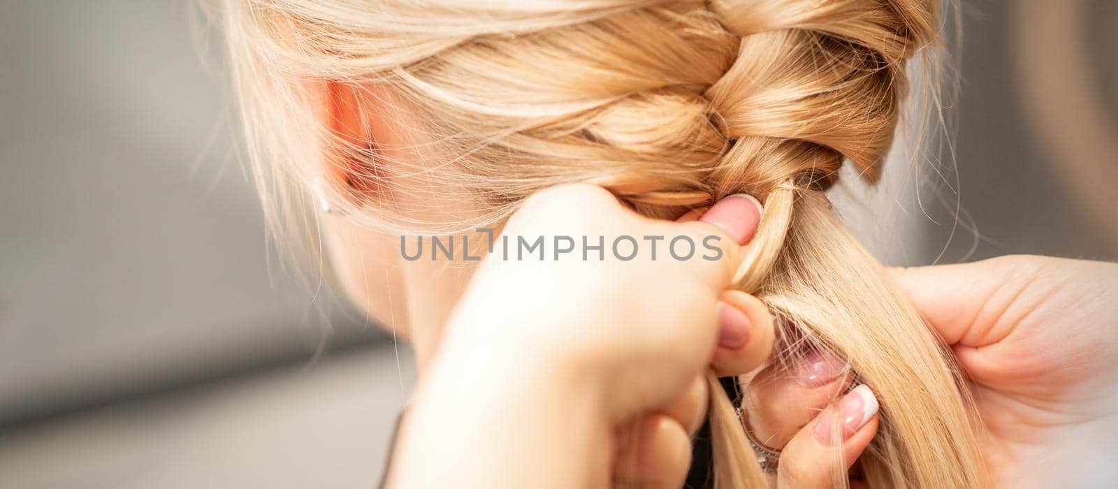 Close up back view of female hands braiding a pigtail to young blond woman at beauty salon