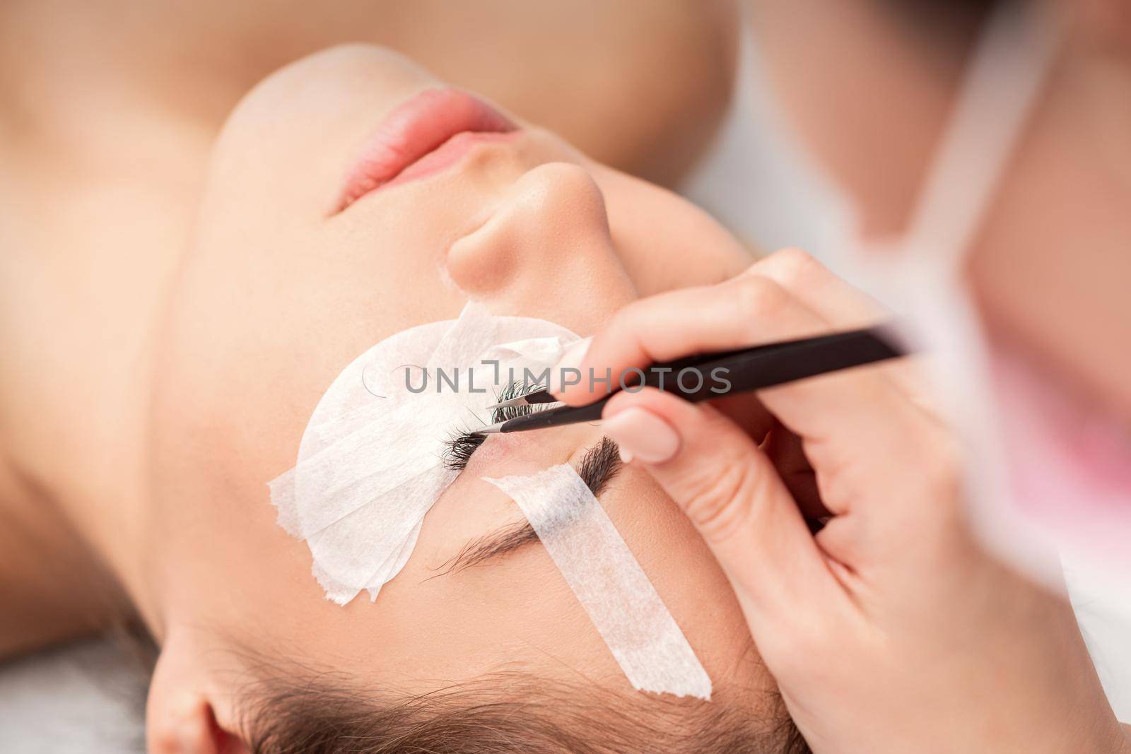 Young caucasian woman receiving eyelash extensions procedure in beauty salon