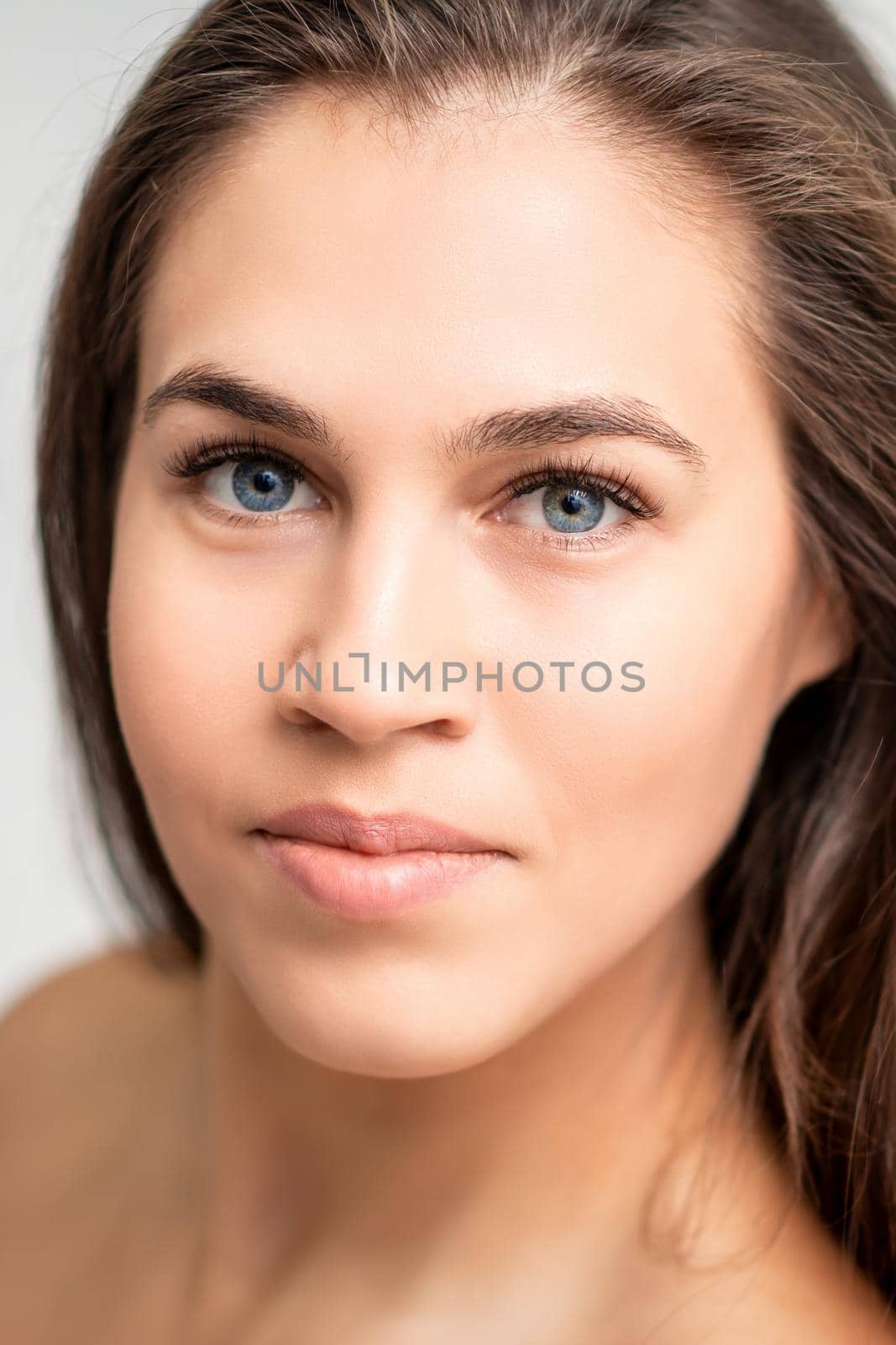 Face portrait of young caucasian woman with natural make up and eyelash extensions looking at camera on white background