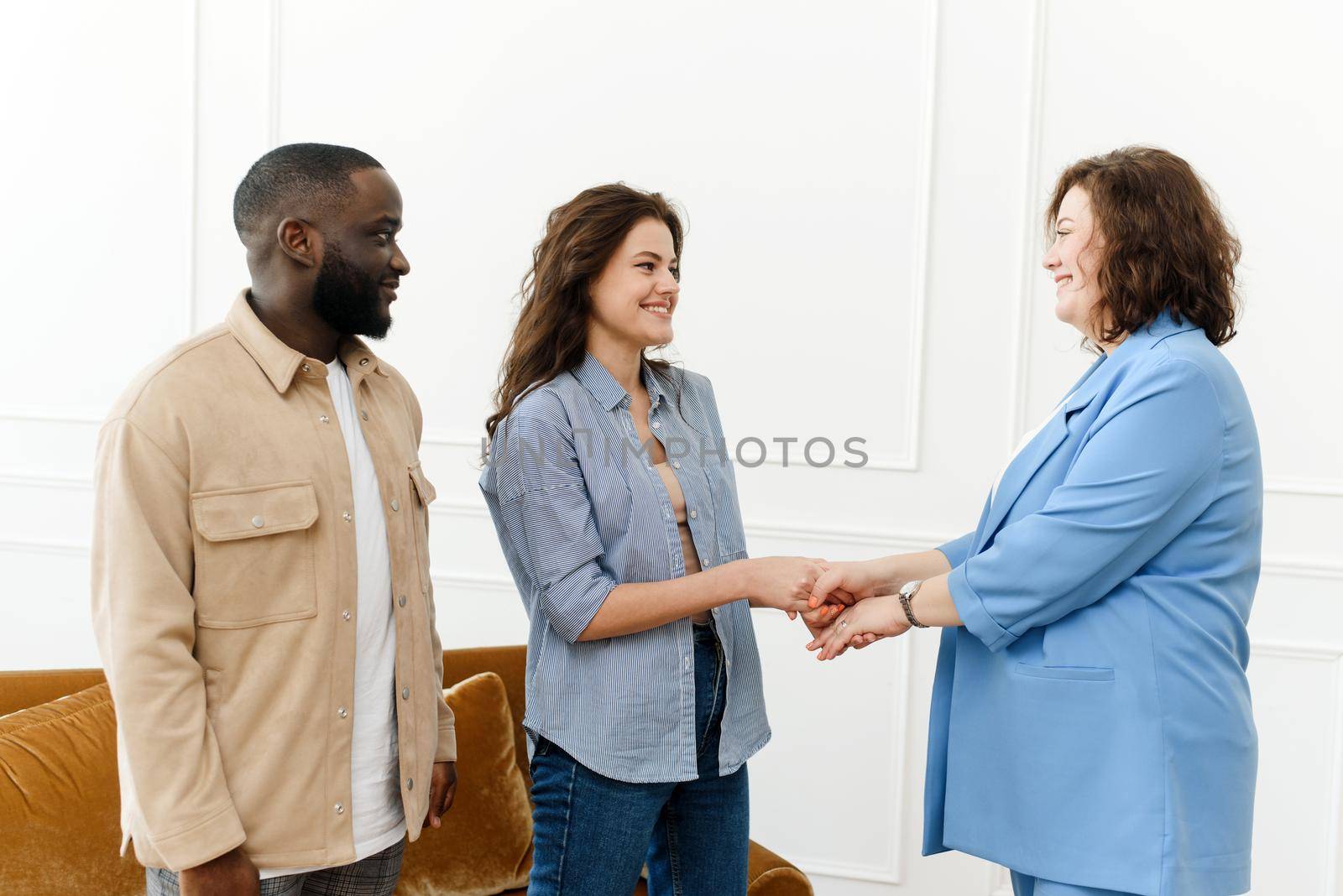 Female family psychologist shakes hands with a young woman. Young Diverse Couple Thanks Psychologist for Successful Session and Saved Marriage