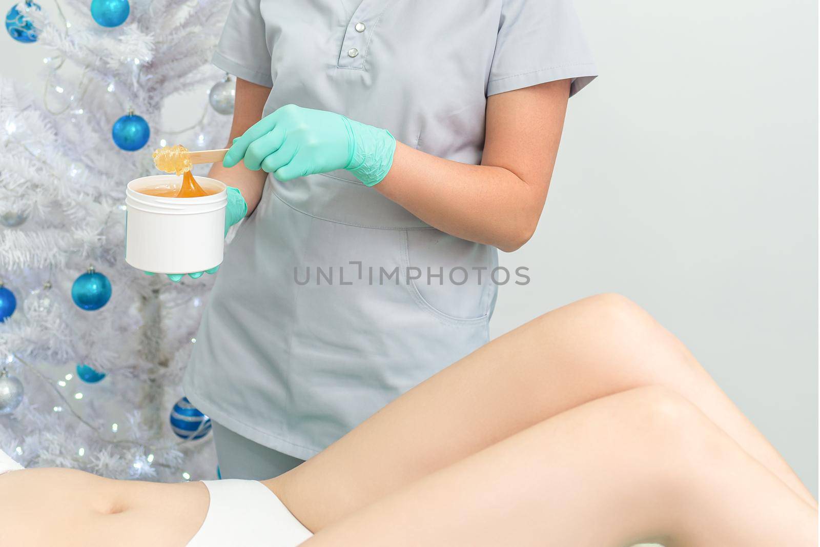 Female cosmetologist holding white blank jar with sugaring paste on christmas tree background