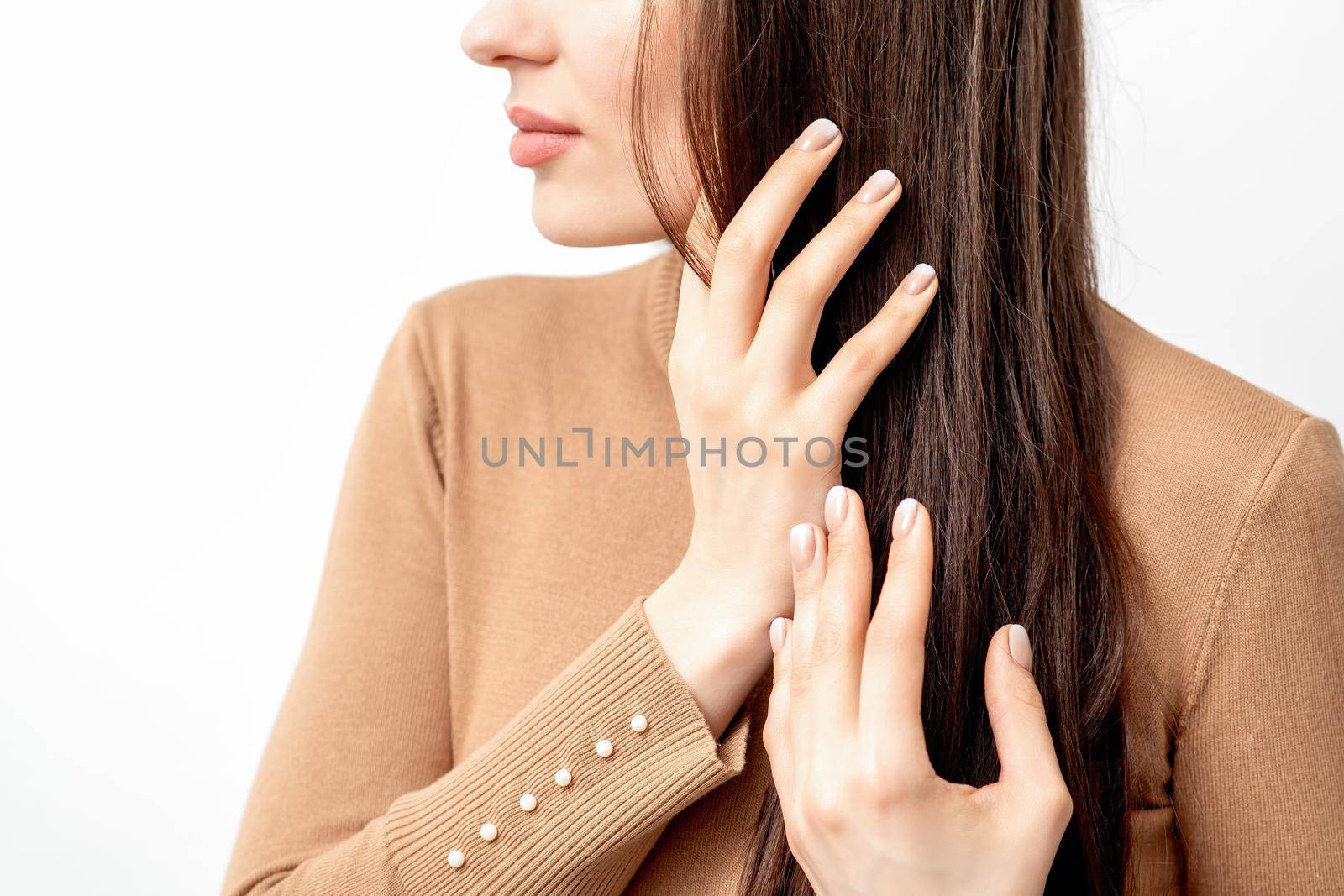 Side view portrait of beautiful young caucasian brunette woman touching her hair by manicured fingers on white background