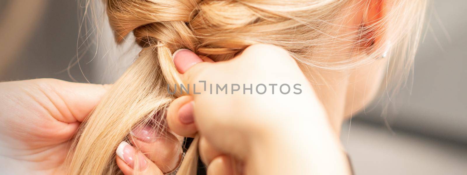 Close up back view of female hands braiding a pigtail to young blond woman at beauty salon