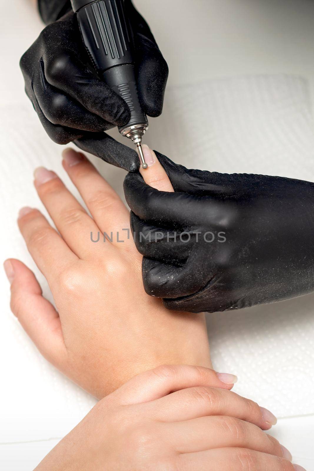 Professional manicure master in black gloves is removing the cuticle by special electric drill manicure tool in beauty salon