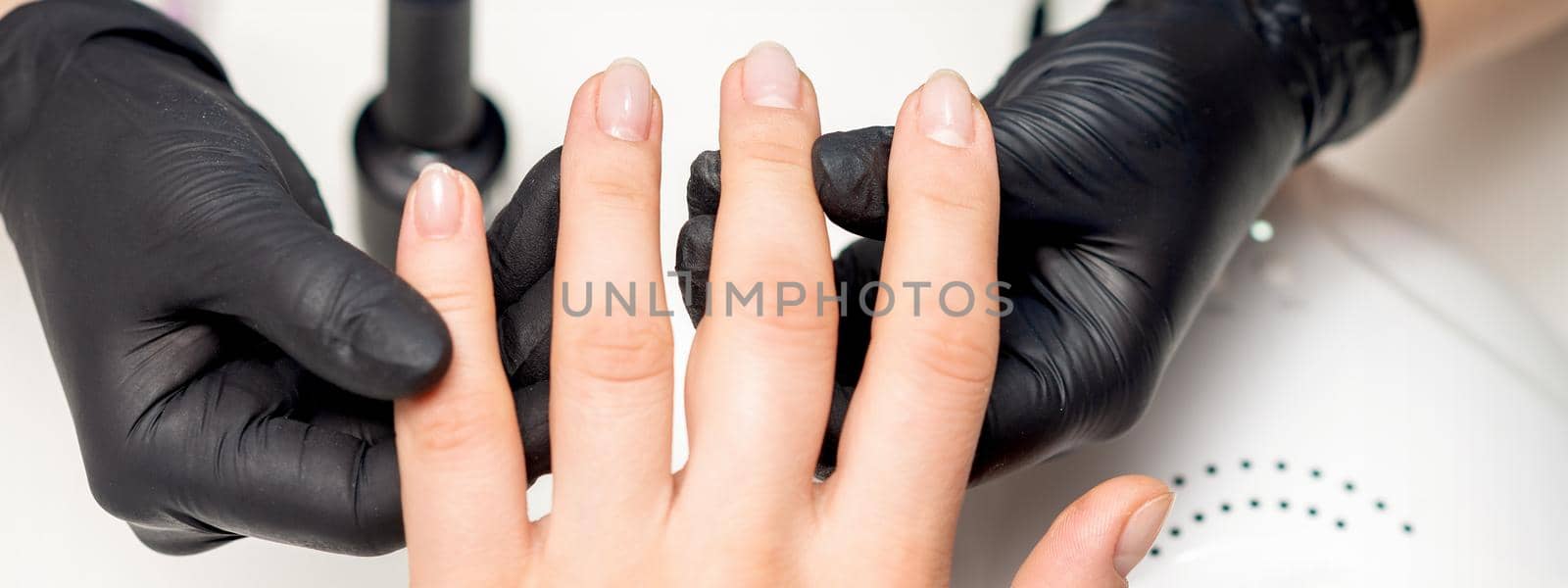 Top view close up of hands of manicurist in sterile black gloves holding client fingers in manicure salon