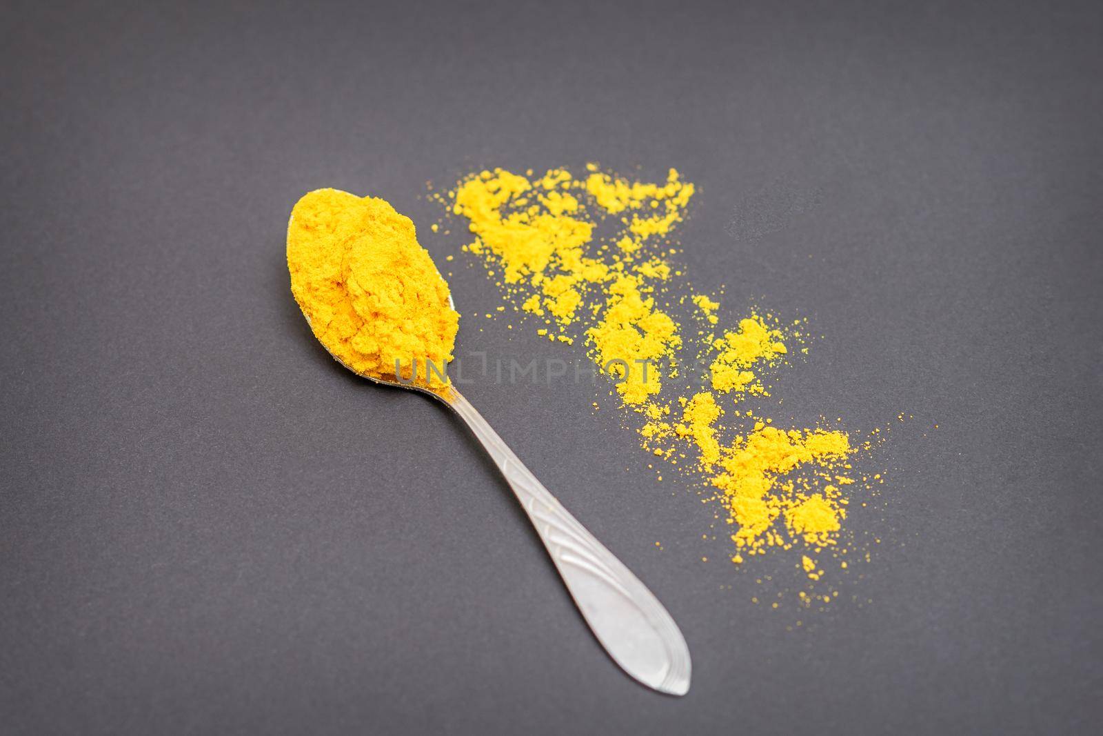 Top view of turmeric or curcuma powder on metal spoon and scattered on dark background.