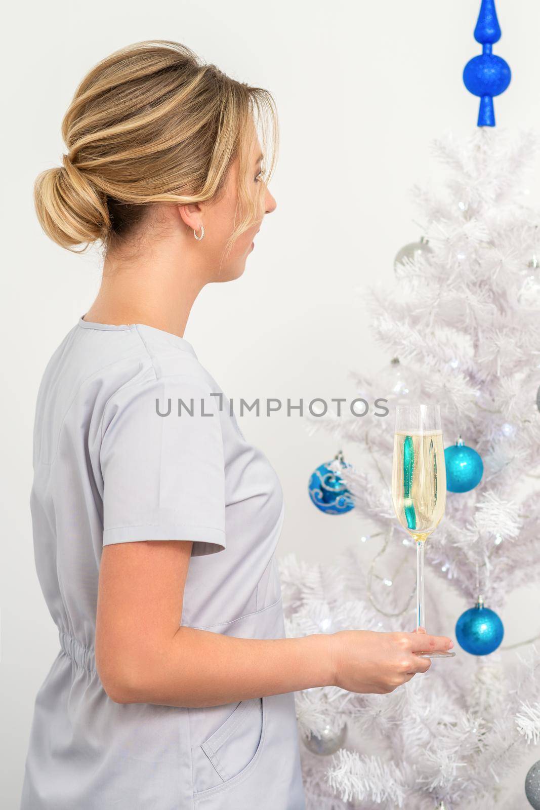 Female doctor with glass of champagne standing near the christmas tree