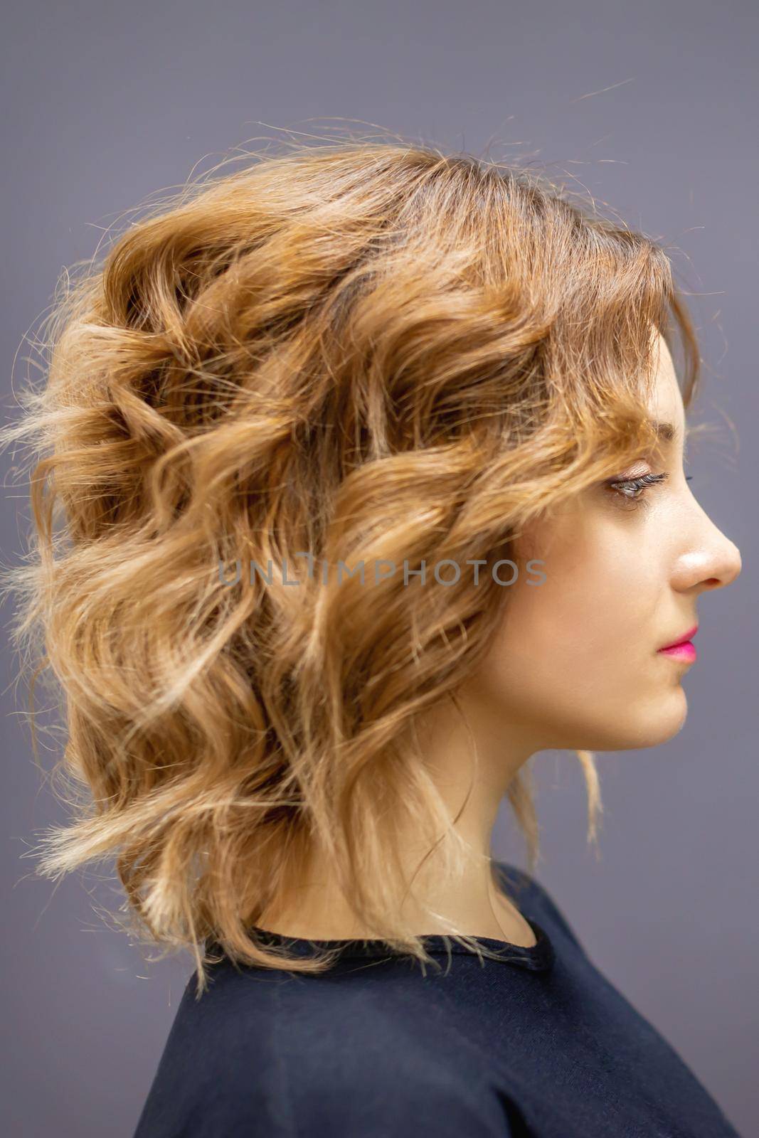 Side view portrait of the beautiful young caucasian woman with red long wavy hairstyle on dark gray background