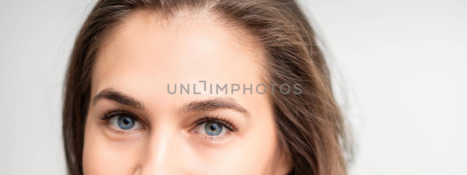 Half face portrait of young caucasian woman with natural make up and eyelash extensions looking at camera on white background
