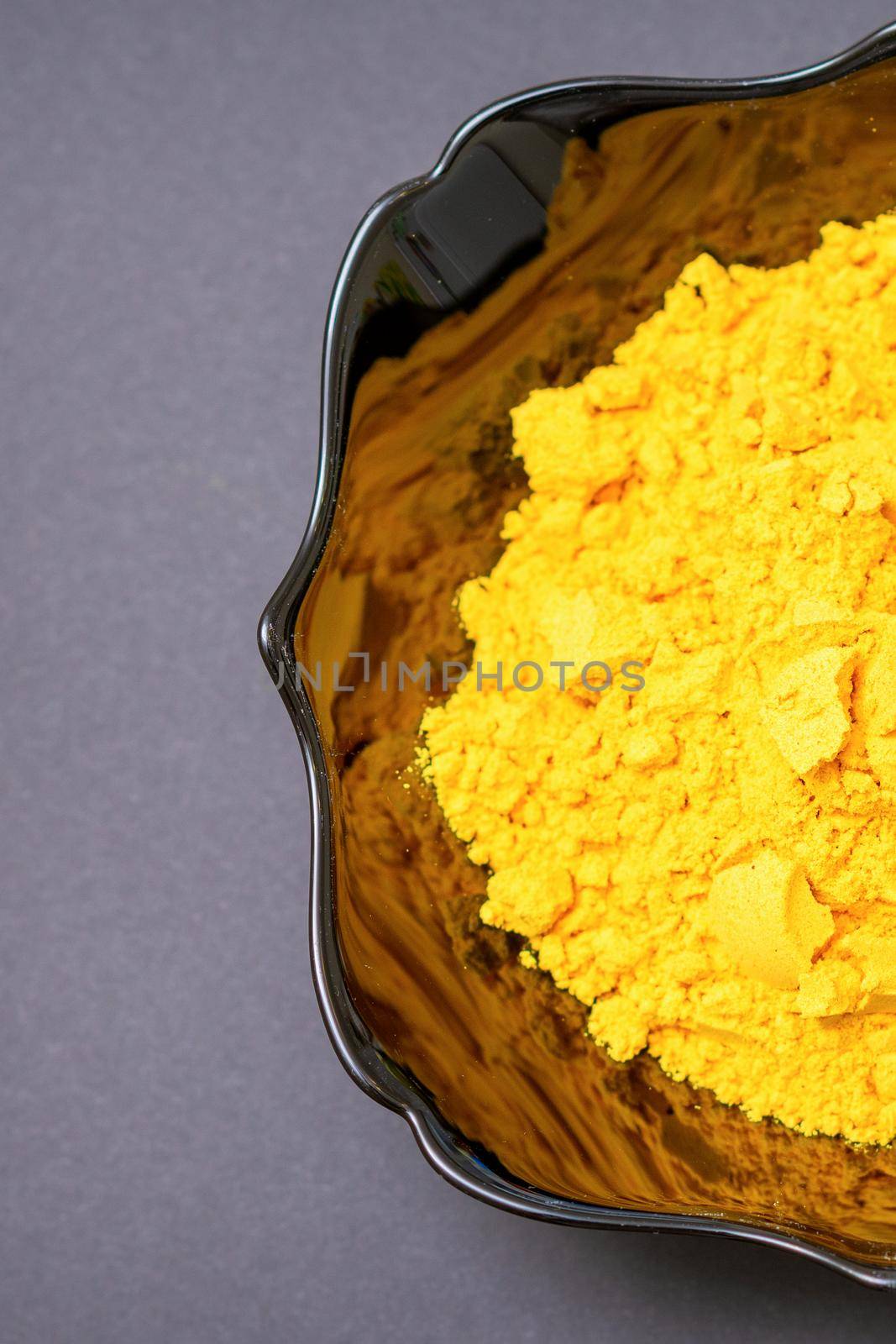 Top view closeup of turmeric or curcuma powder in ceramic black bowl or deep plate on dark background. Flat lay