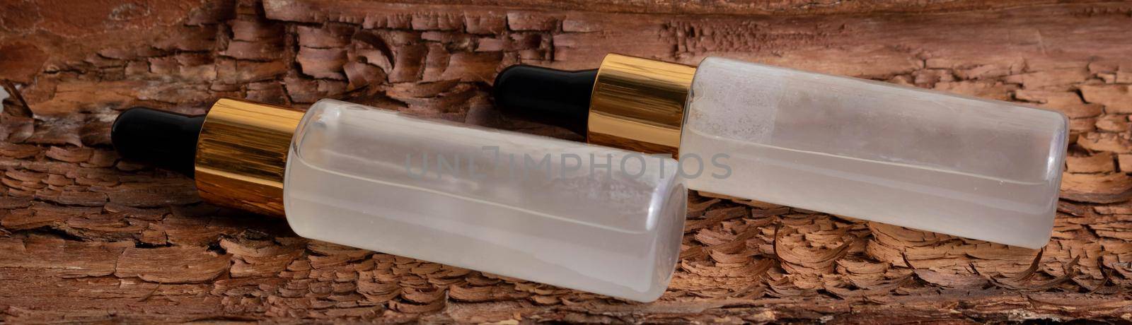 Vials of serum with a pipette lie against a background of brown bark. A close-up of a frosted glass container for a cosmetic skin care product. by lapushka62