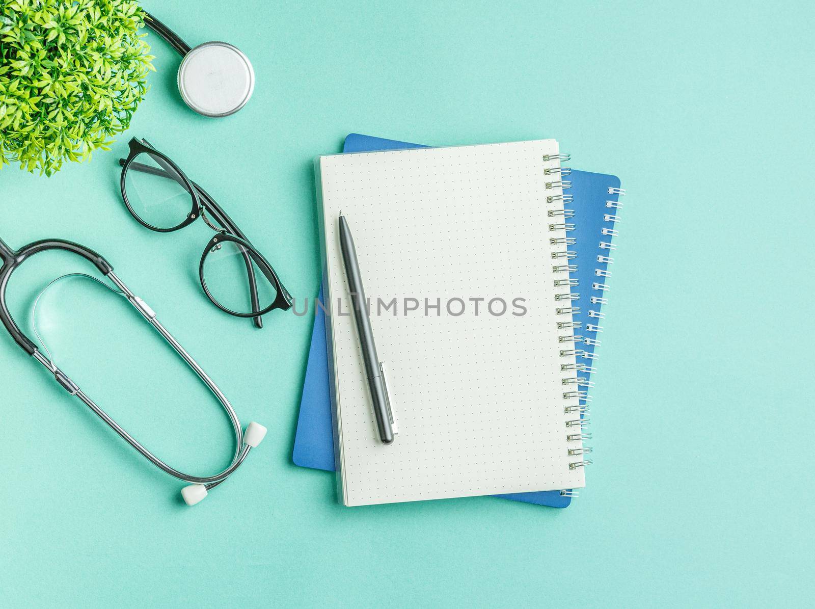 Open notebook with a pen and glasses on a green hospital background flat lay. top view. Nurse workplace concept. Stethoscope on the doctor work desk.