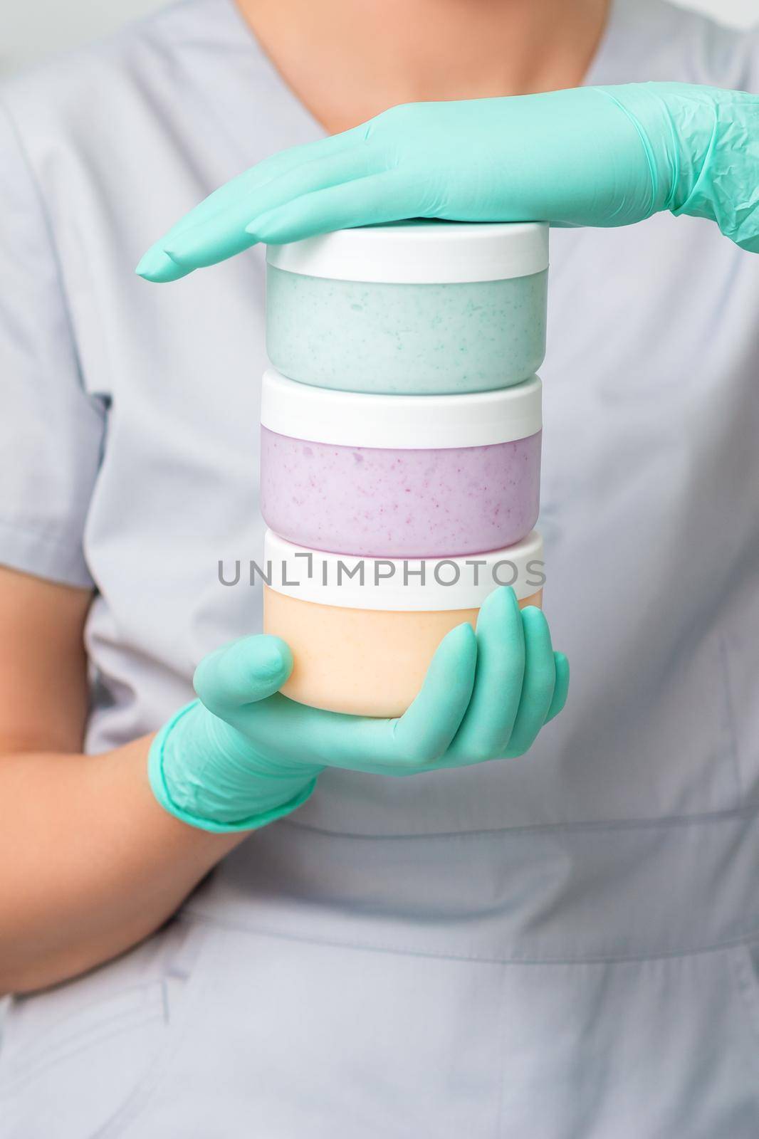 Three colored plastic jars in hands of female cosmetologist in protective gloves