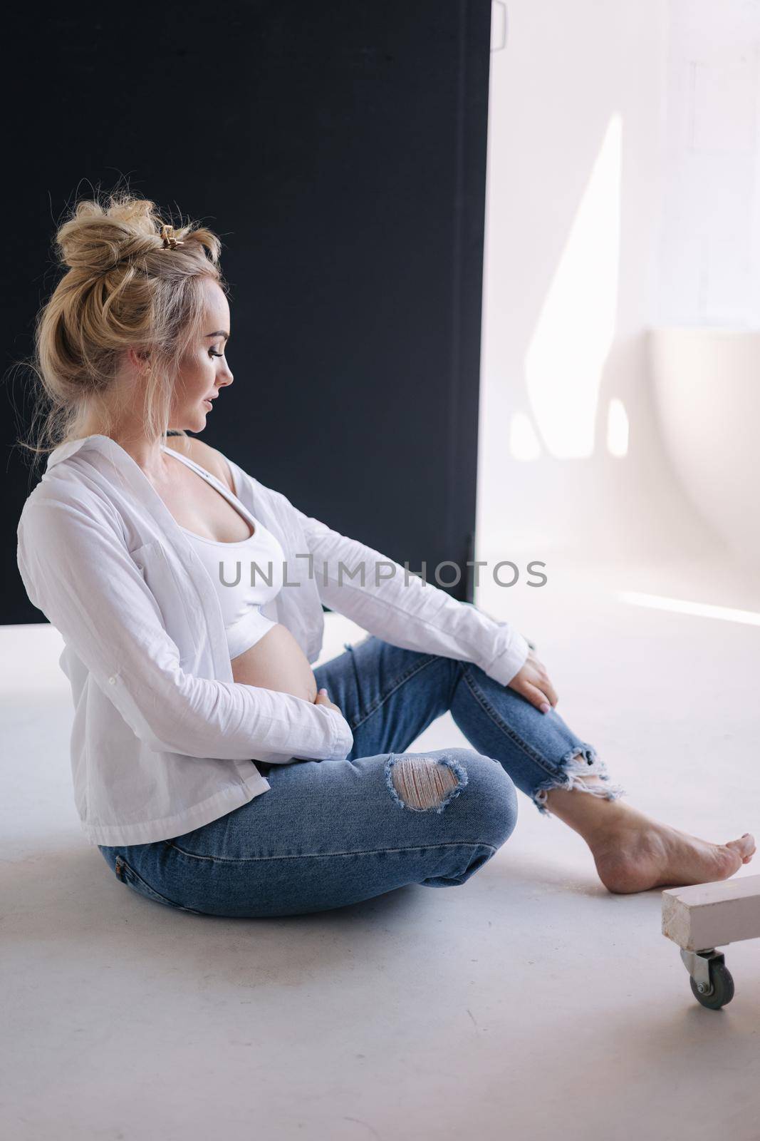 Close up portrait of pregnant woman in studio on white background. Beautiful future mother put her her hands on her belly. Stylish woman in white jaket