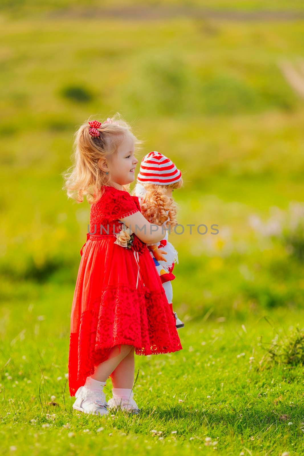 girl in a red dress and with a doll in her hands stands in nature