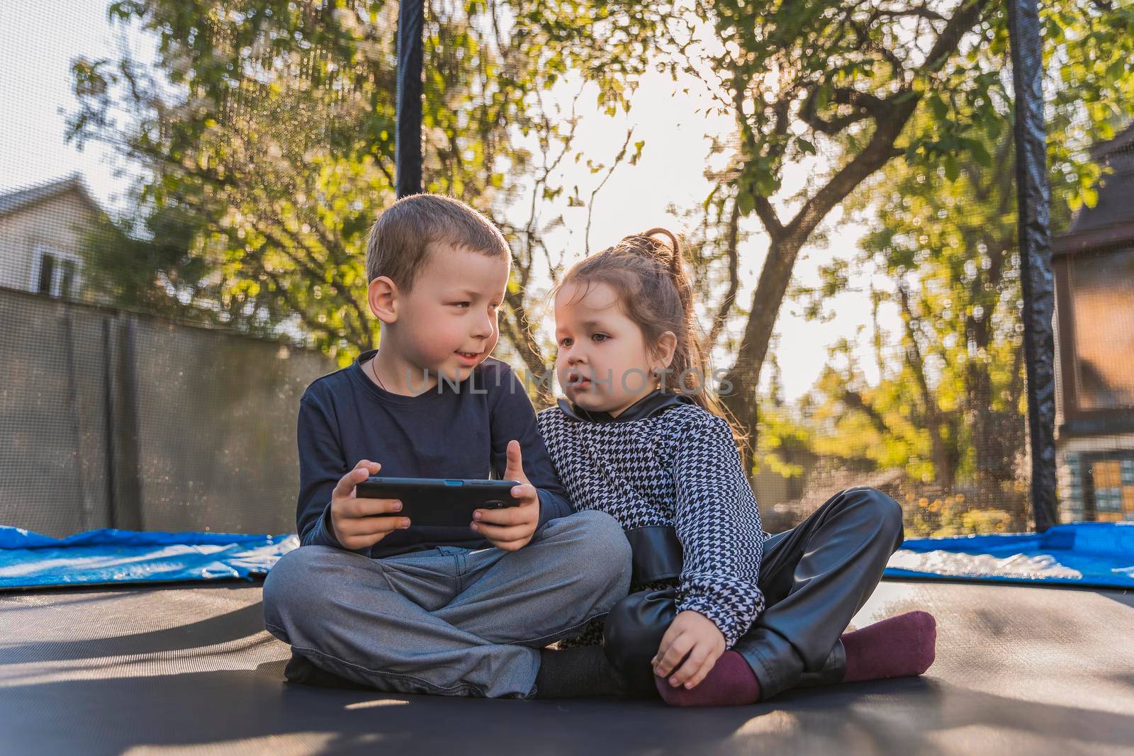 children sitting on a trampoline looking at the phone by zokov