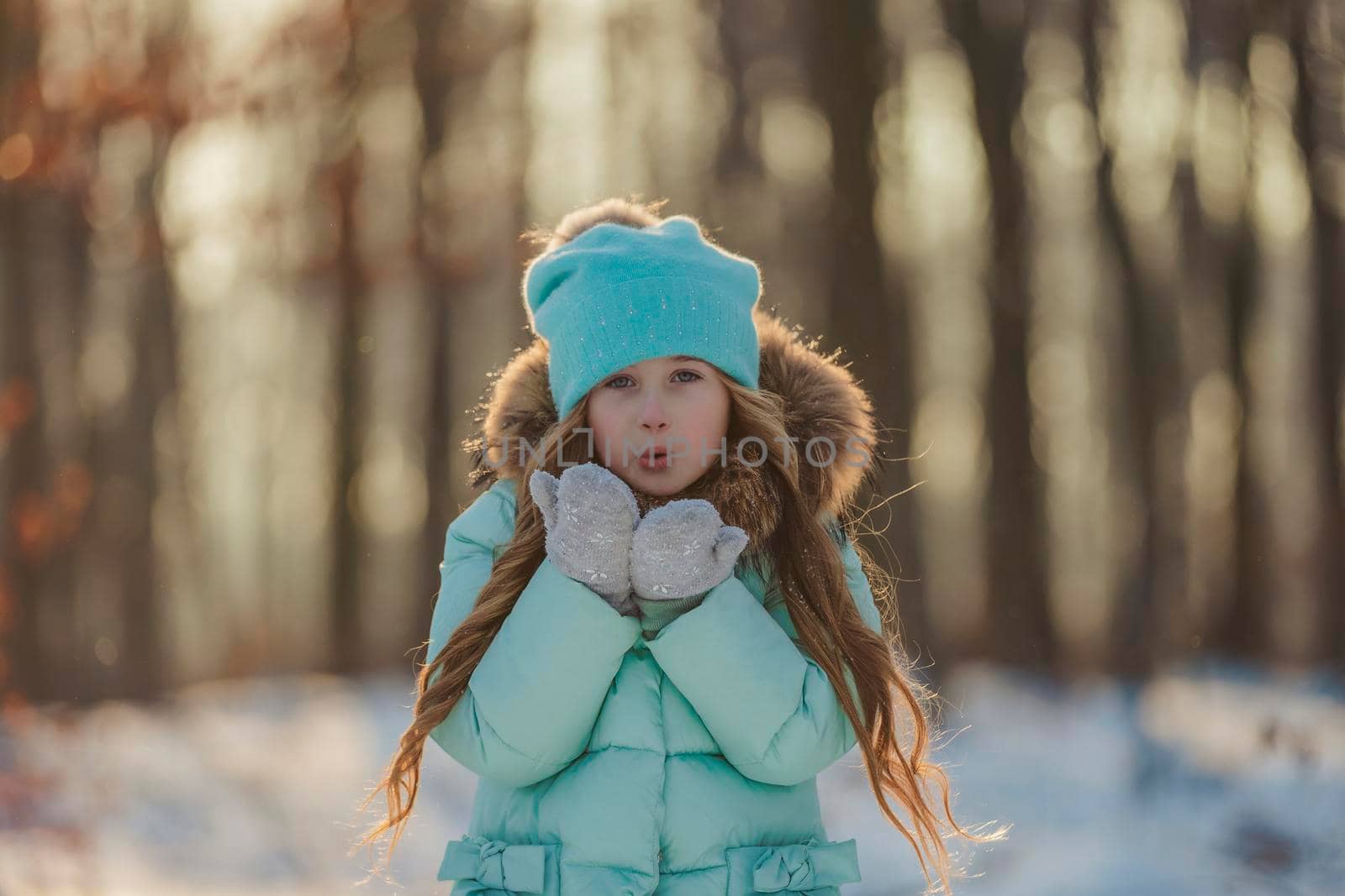 little girl blows on the snow that is on her mittens