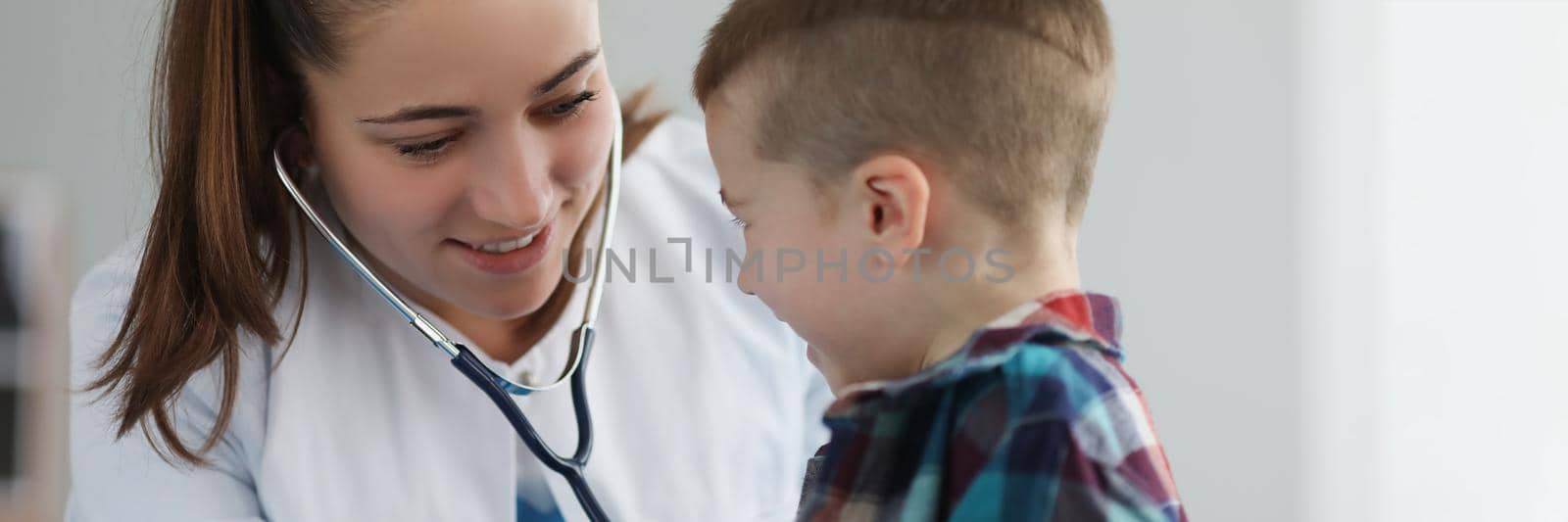 Young woman pediatrician listen kid with stethoscope tool on planned checkup by kuprevich