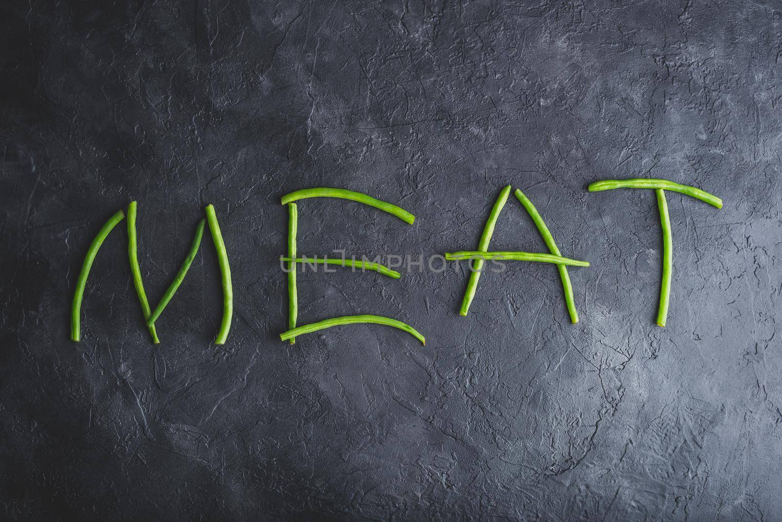 Word Meat Spelled Out In Fresh Pods of Green Beans on Dark Concrete Background