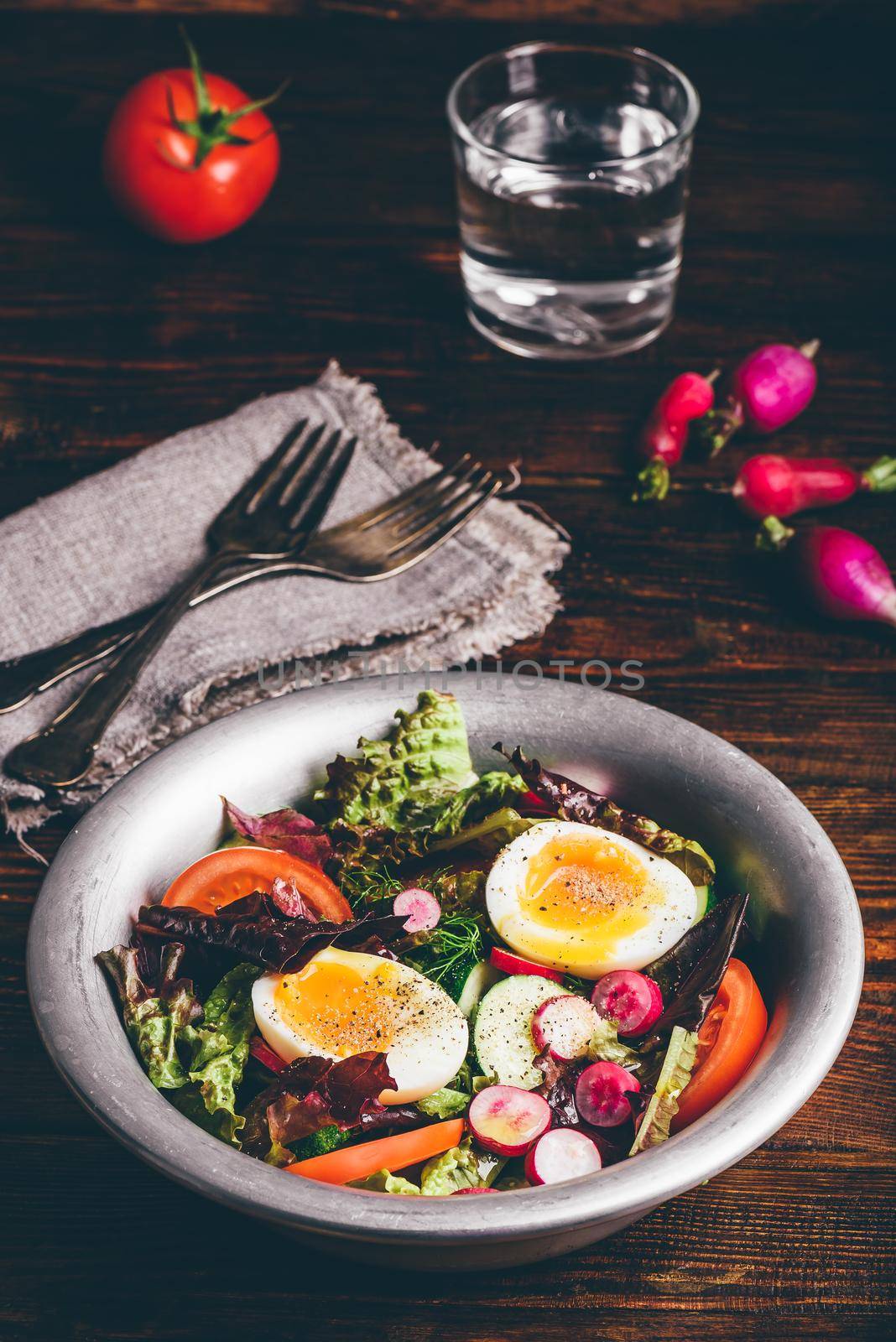 Fresh spring salad with tomato, radish, cucumber, red leaf lettuce and boiled eggs in metal bowl