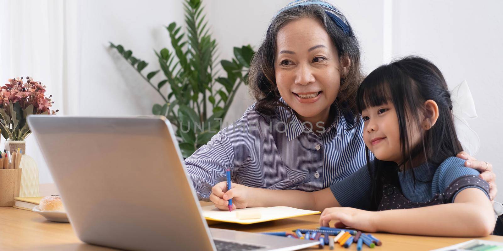 Asian grandmather teach granddaughter drawing and doing homework at home. by wichayada