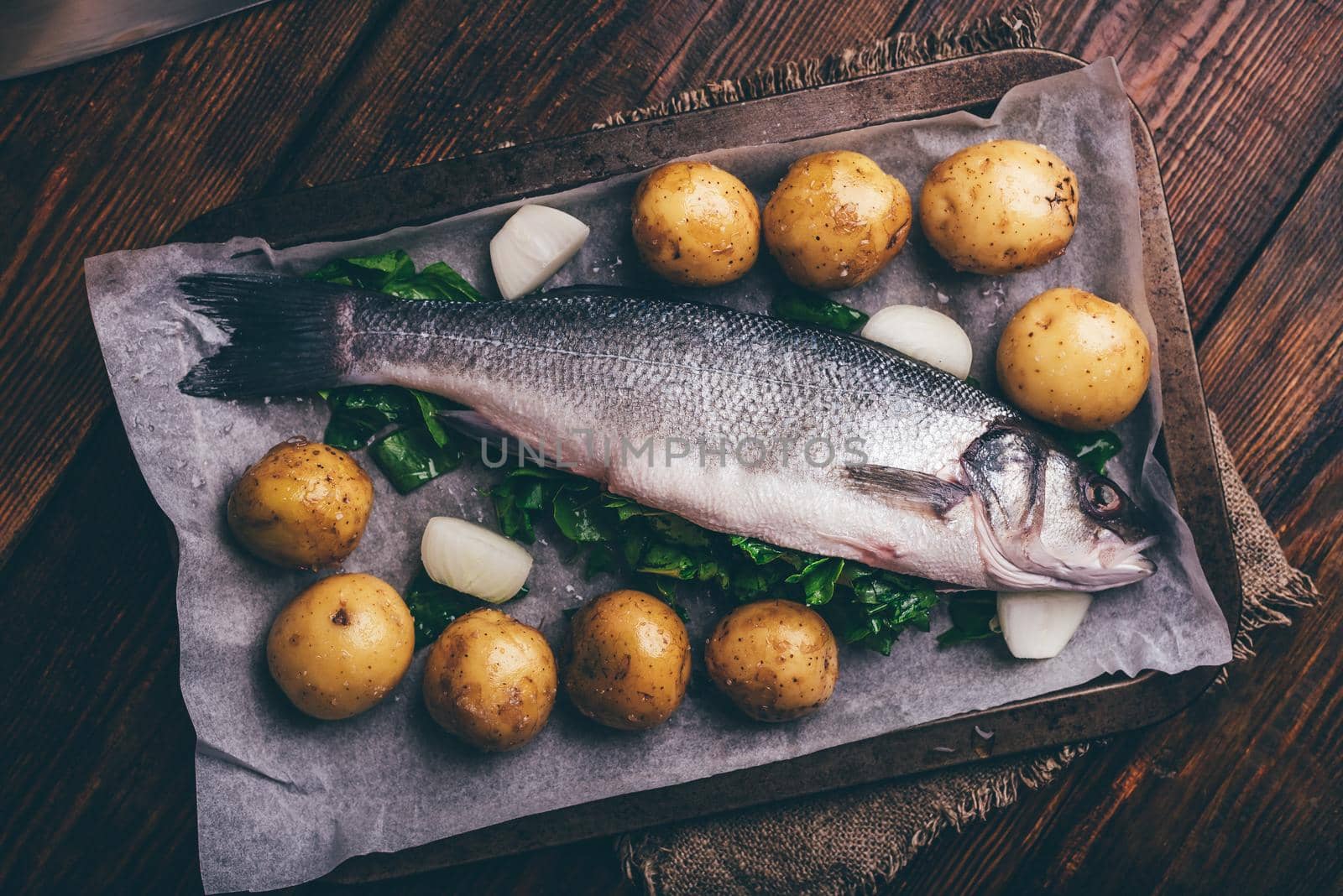 Fresh Sea Bass Stuffed with Sorrel Ready to Be Cooked with New Potatoes and Onion, Lying on Baking Sheet. View from Above