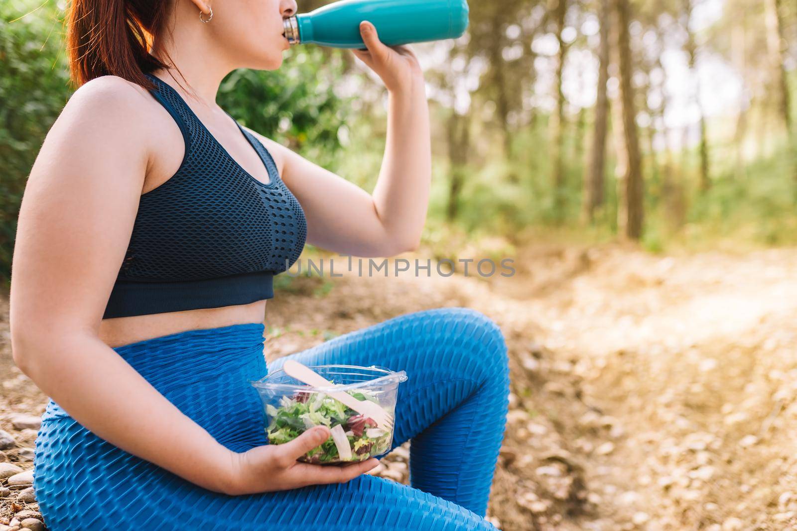 cropped shot of young sportswoman sitting drinking and eating healthy after sports training. girl playing sport outdoors. health and wellness lifestyle. by CatPhotography