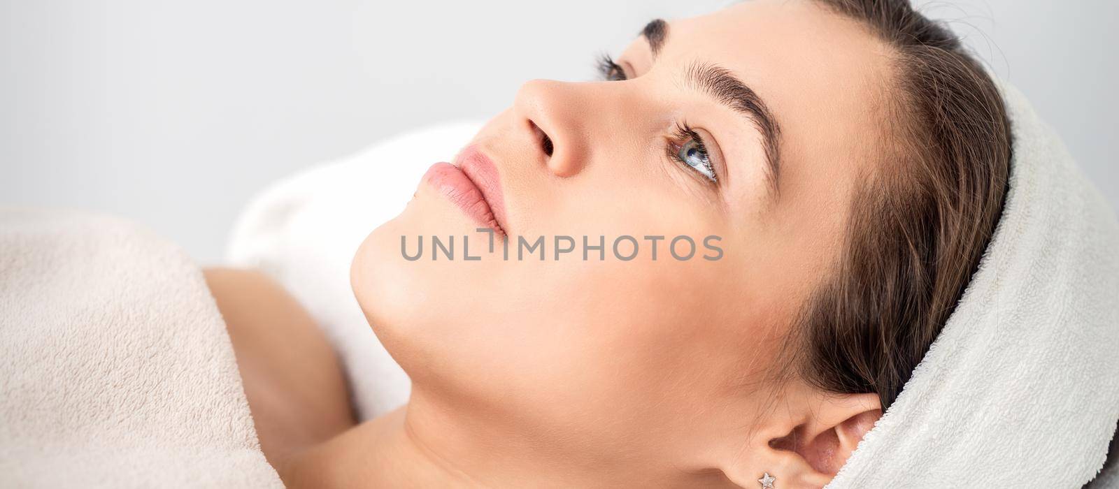 Side view portrait of pensive young woman lying on beautician table while waiting for cosmetic procedure in beauty salon