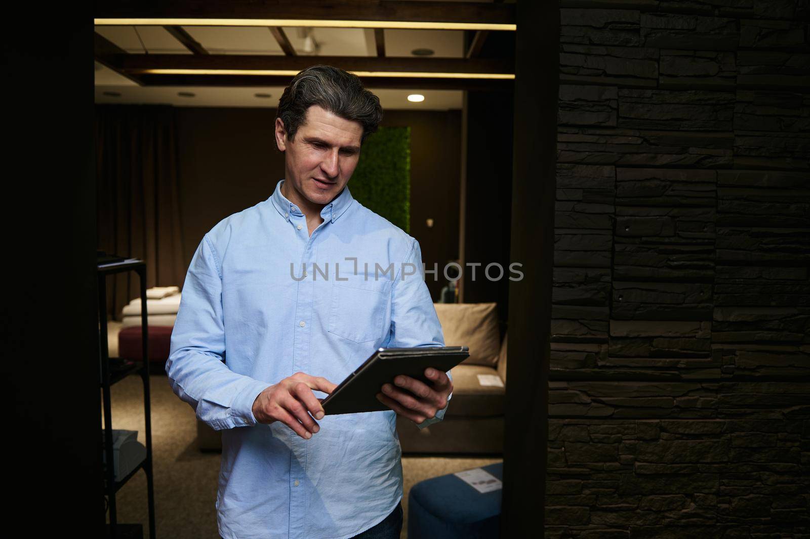 Confident pleasant mature Caucasian man- sales manager , real estate agent, retail assistant using digital tablet works in a furniture design store. Interior design, small business concept