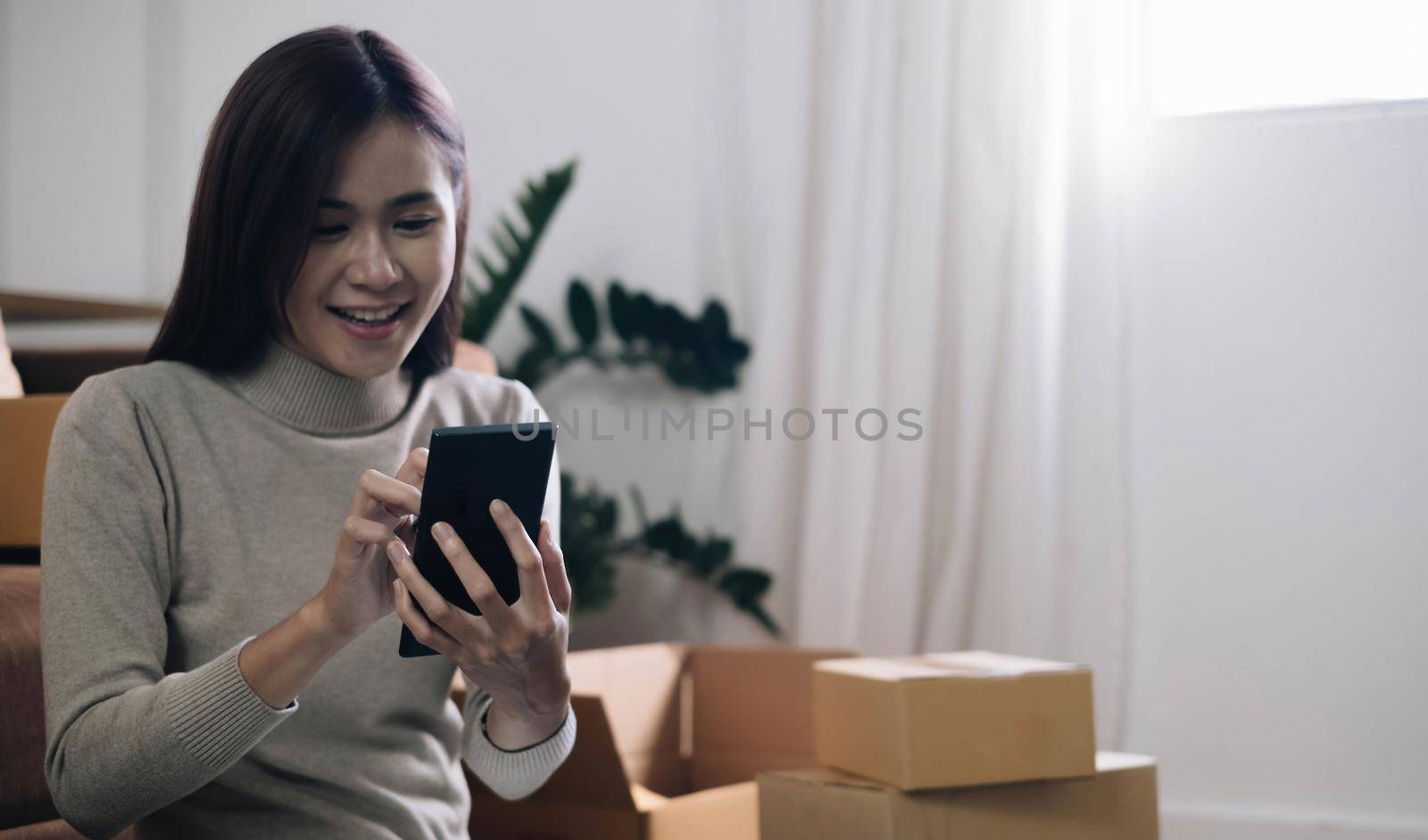 Starting Small business entrepreneur SME freelance,Portrait young woman working at home office, BOX,smartphone,laptop, online, marketing, packaging, delivery, SME, e-commerce concept by wichayada