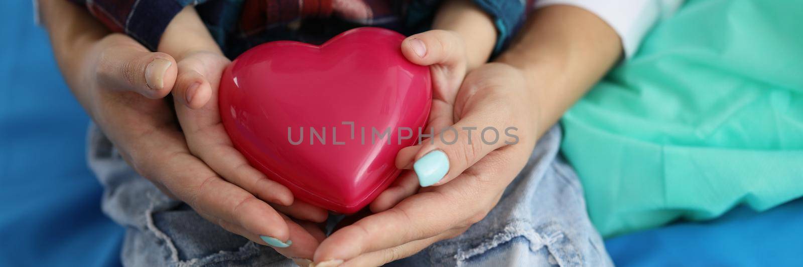 Woman and child holding red heart on palms symbol of love by kuprevich