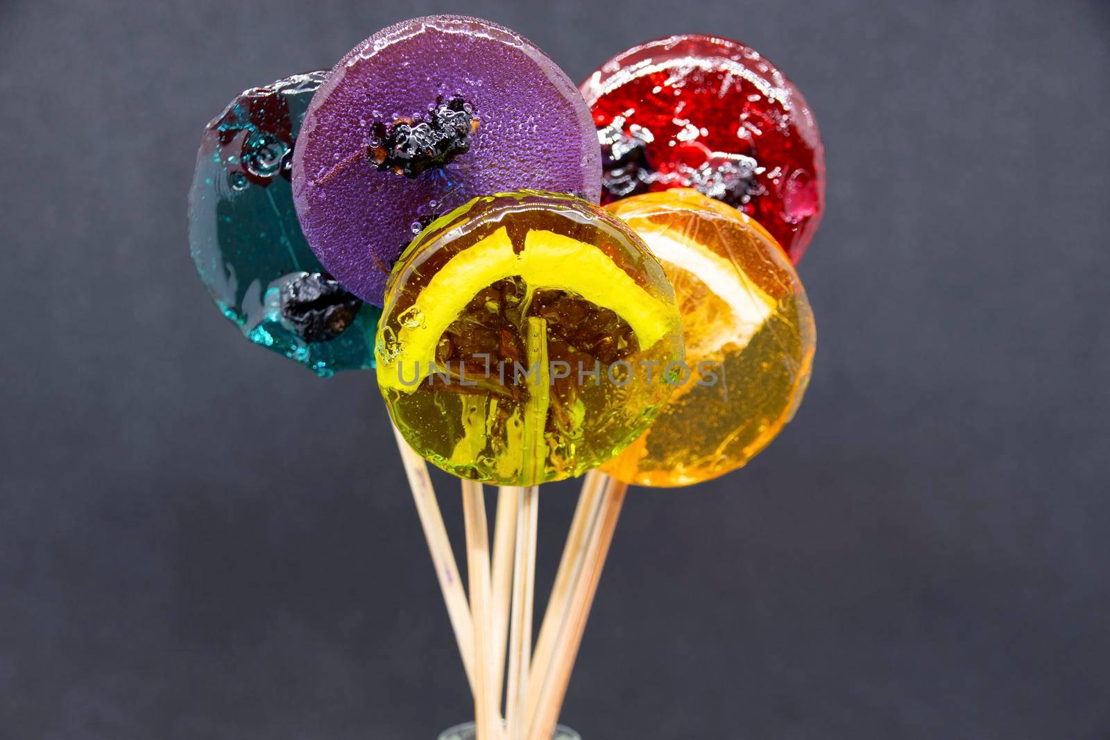 Colored lollipops with different berries and fruits inside close-up on a gray background.