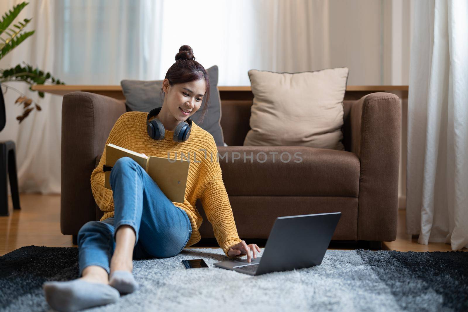 A young female student sitting on floor using headphones and laptop computer for studying. taking note online education