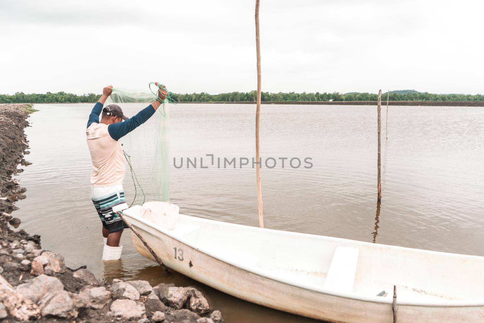 Latin American fisherman checking his net to catch farmed shrimp in his boat in a pond by cfalvarez