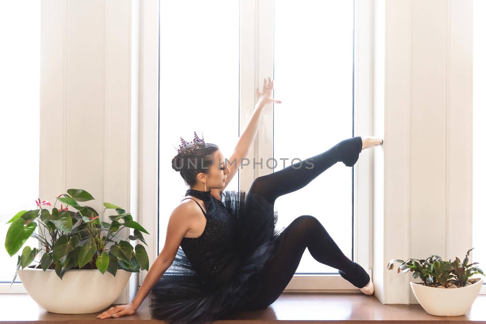 graceful ballerina in black swan dress against white background. Young ballet dancer practicing before performance in black tutu, classical dance studio, copy space