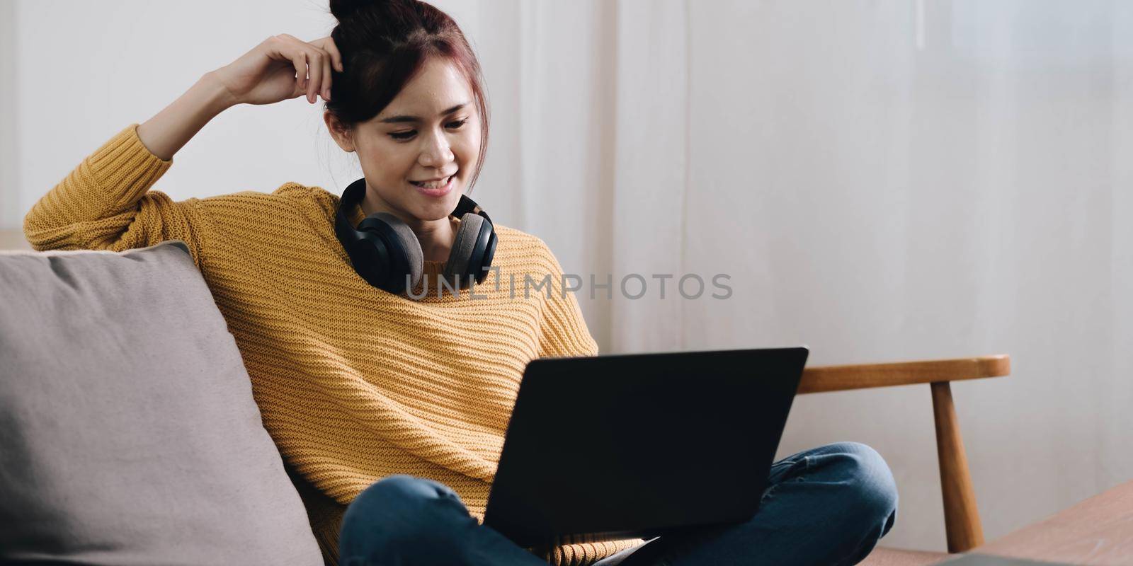 Cheerful freelancer working on laptop sitting on couch and listening to music in headphones, copyspace