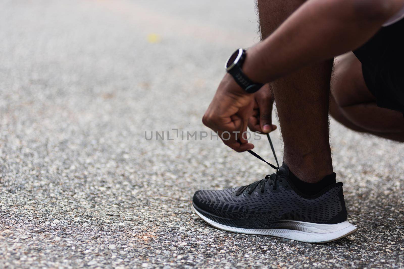 runner black man wear watch sitting he trying shoelace running shoes by Sorapop