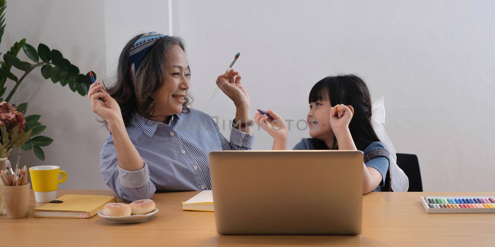 Asian grandmother and granddaughter happily pencil drawing at home.