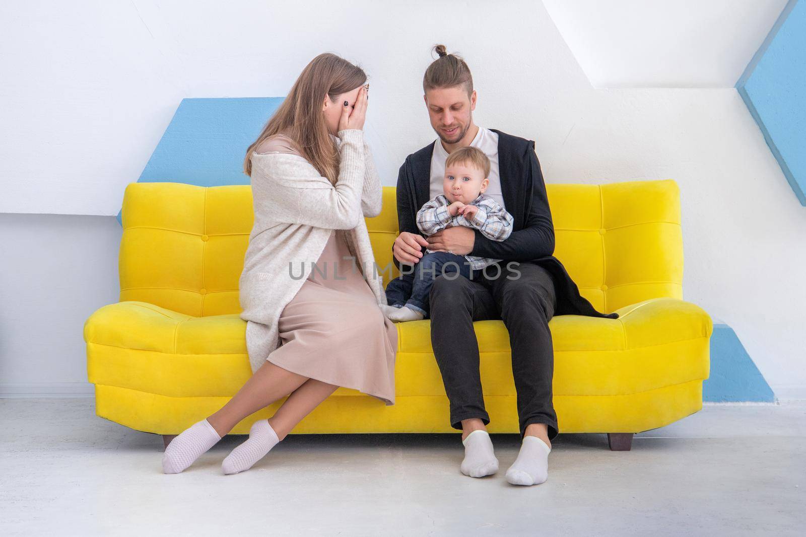 Young caucasian happy family with his little kid having fun on sofa in bright interior by Rom4ek