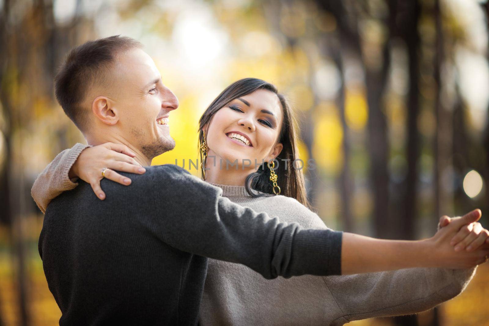 Portrait of a happy asian and caucasian couple of lovers on a date dancing in autumn park by Rom4ek