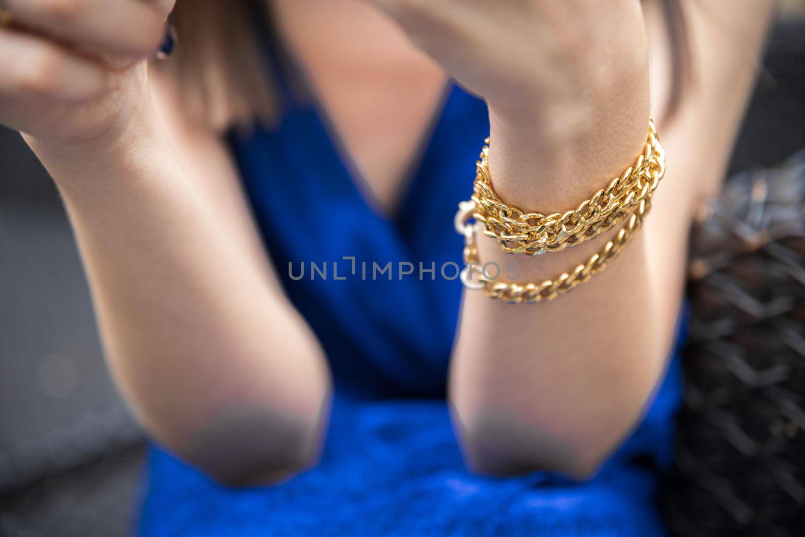 Bracelet in the form of a chain on the wrist of a woman in a blue dress.