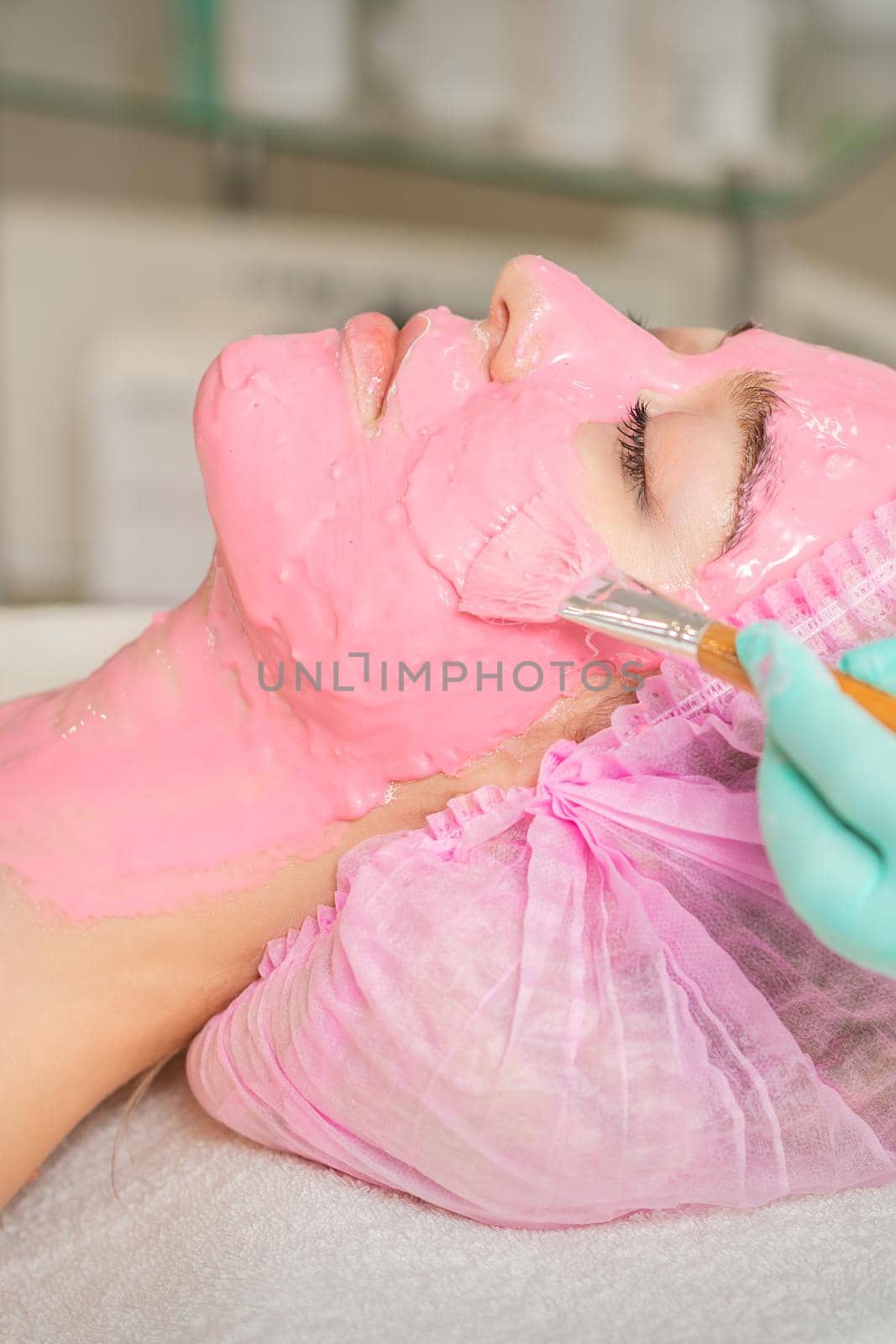 Cosmetologist applying pink alginic mask by okskukuruza