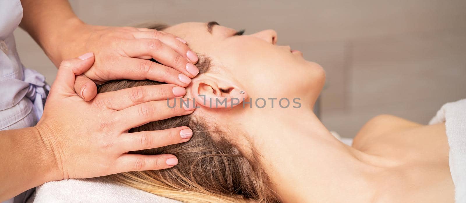 Young woman receiving head massage by hands of beautician in spa beauty center