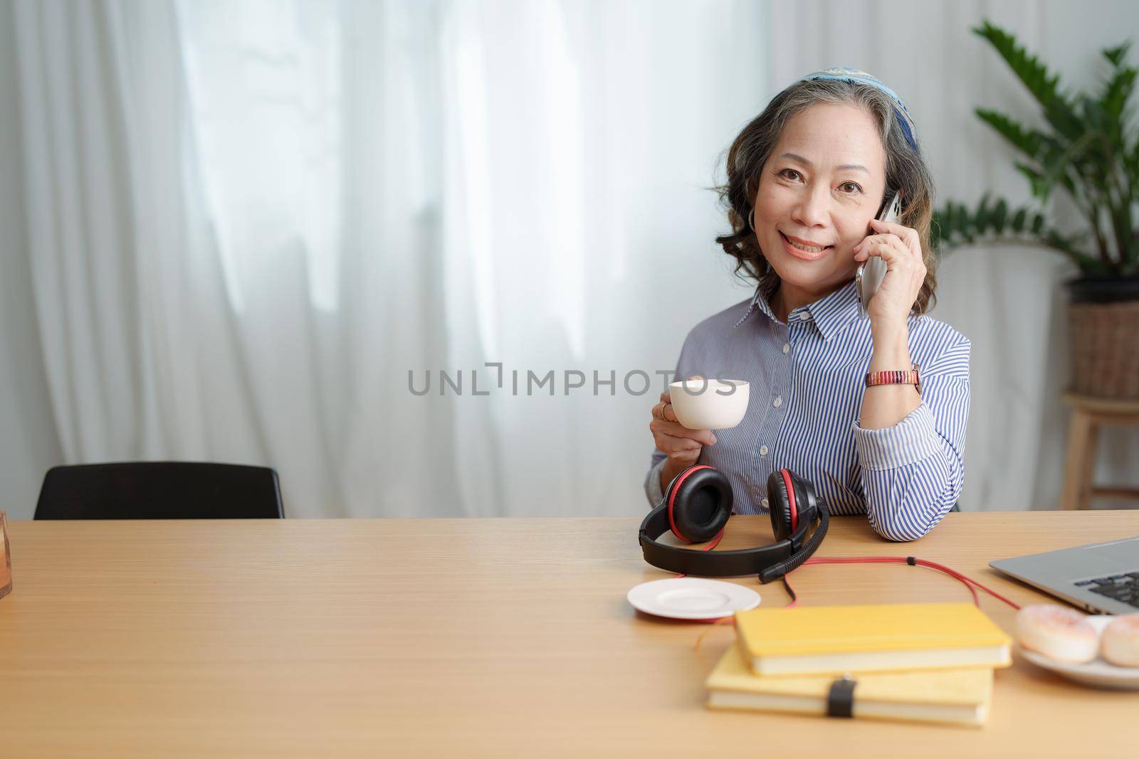 Portrait of an elderly woman talking to a friend on the phone during a coffee break by Manastrong