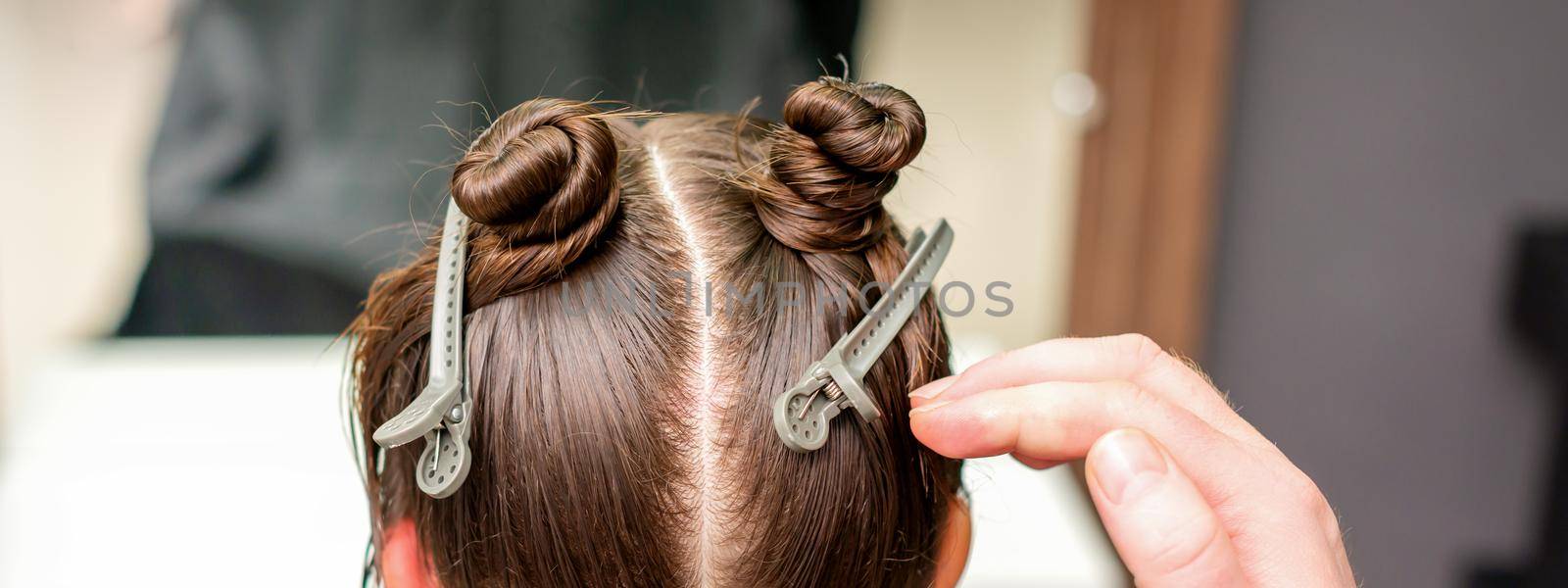 Rear view of hand of hairdresser doing haircut of young woman with hair clips on her hair in hair salon